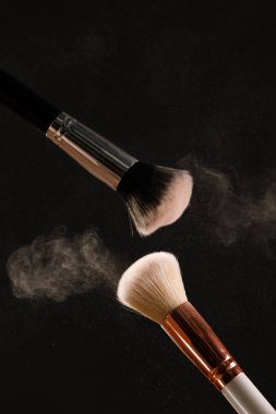 Siyah arka plan üzerine toz allık patlama ile kozmetik fırçalar makyaj. Cilt Bakımı ya da moda kavramı.