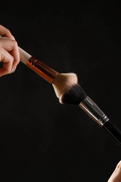 Make up cosmetic brushes with powder blush explosion on black background. Skin care or fashion concept.