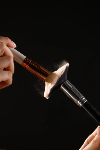 Make up cosmetic brushes with powder blush explosion on black background. Skin care or fashion concept.