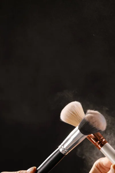Make up cosmetic brushes with powder blush explosion on black background. Skin care or fashion concept.