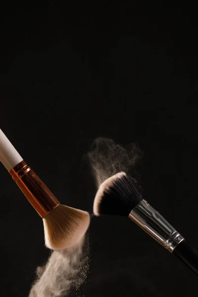 Make up cosmetic brushes with powder blush explosion on black background. Skin care or fashion concept.