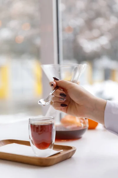 Una taza de té, un platillo, una rama de una planta viva, una mandarina anaranjada.Ambiente invernal con velas — Foto de Stock