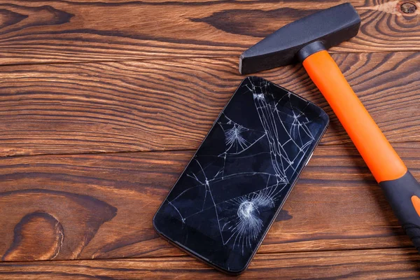 The touch screen of the smartphone is broken with a hammer, the concept of a device failure.Smartphone with a broken touch screen and a hammer on a wood background, break the device