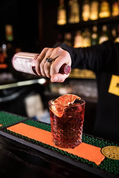 Expert barman is making cocktail at night club.bartender with cocktail and orange peel preparing cocktail at bar. alcohol drinks, people and luxury concept