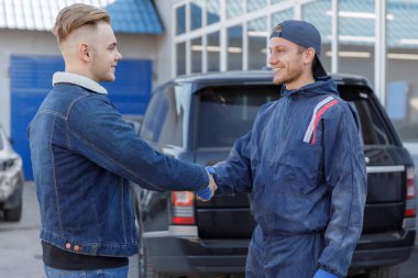 Araba Servisi, tamir, anlaşma ve insanlar kavramı - mekanik ve müşteri ya da araba sahibi bir atölyede el sallıyor. Önden Görünüm. Arka planda bir arabadır.