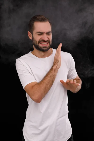 Homem de t-shirt branca no fundo preto fecha nariz — Fotografia de Stock