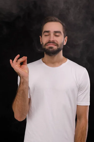 Chico en camiseta blanca inhala humo sobre un fondo negro —  Fotos de Stock