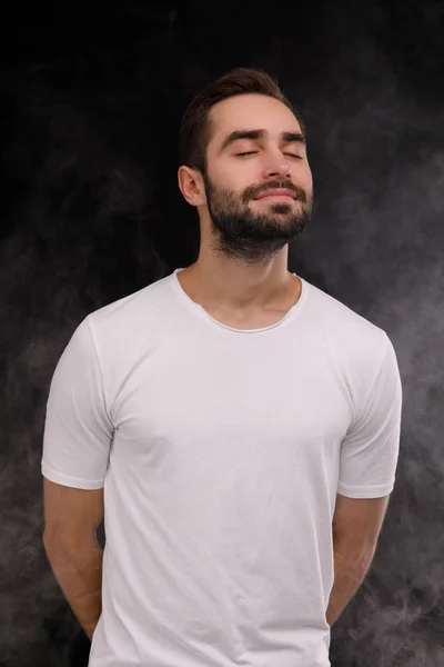 Парень в белой футболке вдыхает дым на черном фоне — стоковое фото