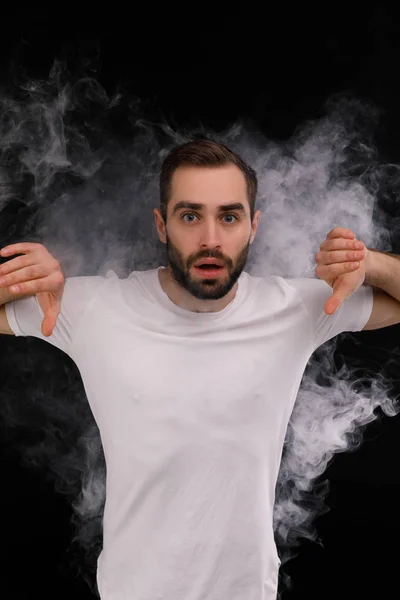 Homem de t-shirt branca sobre fundo preto liberando uma nuvem de fumaça — Fotografia de Stock