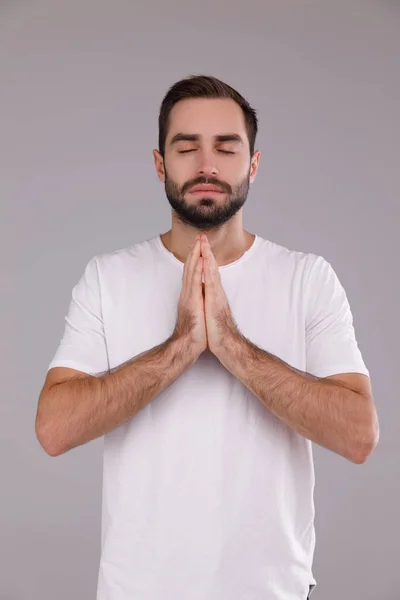 Чоловік з бородою в білій футболці на сірому фоні, молячись — стокове фото