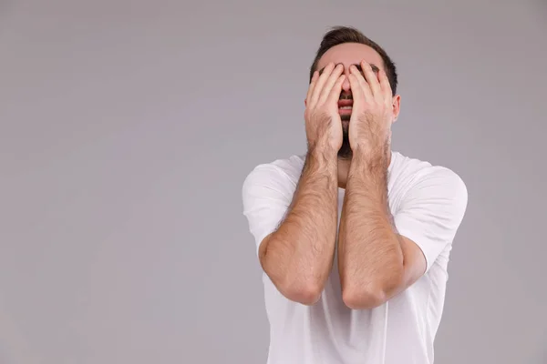 Um homem com uma barba em uma camiseta branca em uma crise de fundo cinza, emoções e conceito de estresse — Fotografia de Stock