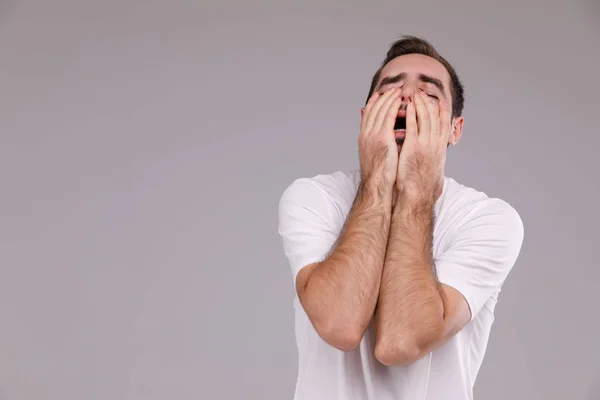 Um homem com uma barba em uma camiseta branca em uma crise de fundo cinza, emoções e conceito de estresse — Fotografia de Stock