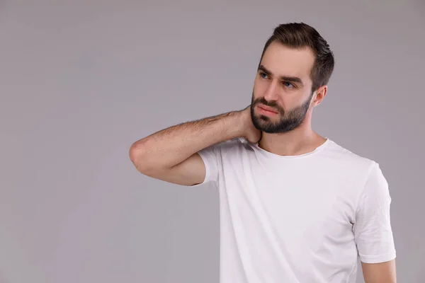 Hombre confundido con barba en camiseta blanca sobre fondo gris —  Fotos de Stock