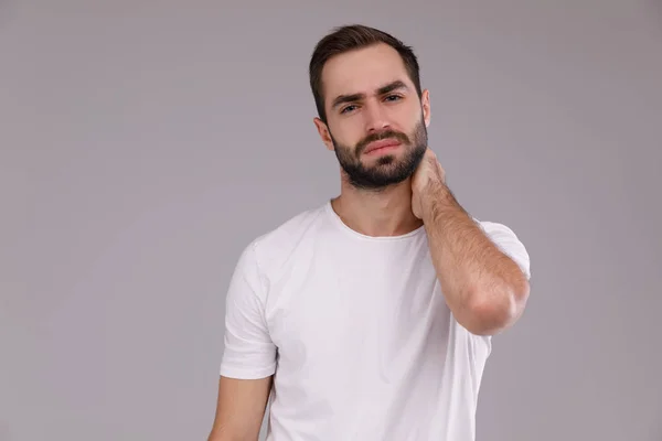 Hombre confundido con barba en camiseta blanca sobre fondo gris —  Fotos de Stock