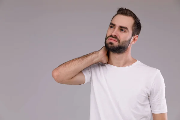 Forvirret mann med skjegg i hvit T-skjorte på grå bakgrunn – stockfoto