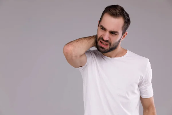 Запутавшийся мужчина с бородой в белой футболке на сером фоне — стоковое фото