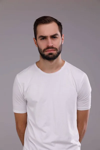 Un hombre con barba en una camiseta blanca sobre un fondo gris —  Fotos de Stock