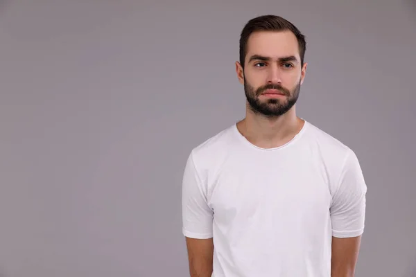Чоловік з бородою в білій футболці на сірому фоні — стокове фото