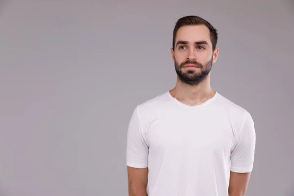 Um homem com uma barba em uma camiseta branca em um fundo cinza — Fotografia de Stock