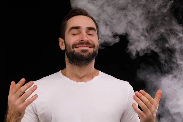 Ο τύπος σε ένα άσπρο t-shirt εισπνέει καπνό πάνω σε μαύρο φόντο — Φωτογραφία Αρχείου