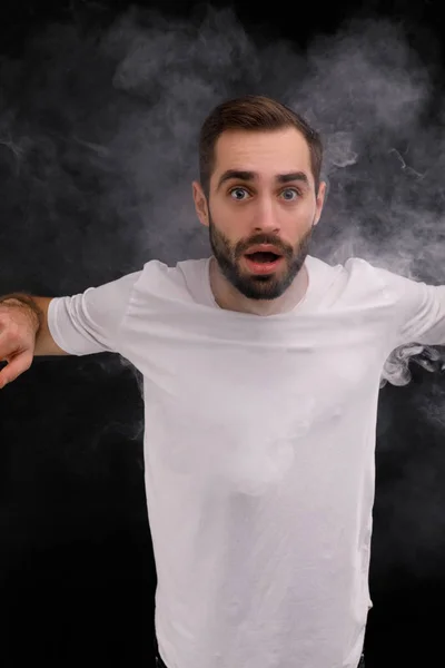 Homem de t-shirt branca sobre fundo preto liberando uma nuvem de fumaça — Fotografia de Stock