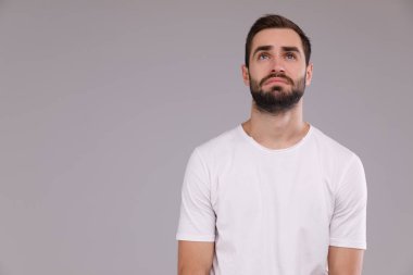 Gri bir arka plan üzerinde beyaz bir T-shirt bir adam portresi. ararken.