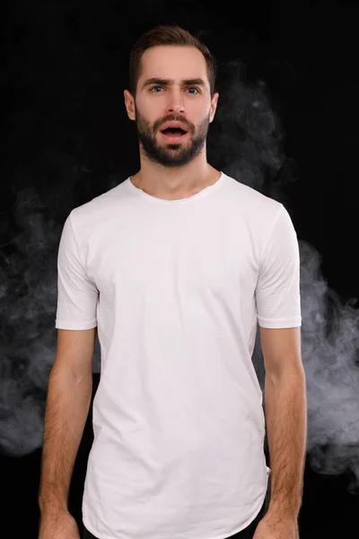 Молодой парень в белой футболке на черном фоне с дымом — стоковое фото
