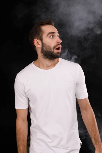 一个穿着白色 t恤的年轻人, 黑色的背景和浓烟望着一旁 — 图库照片