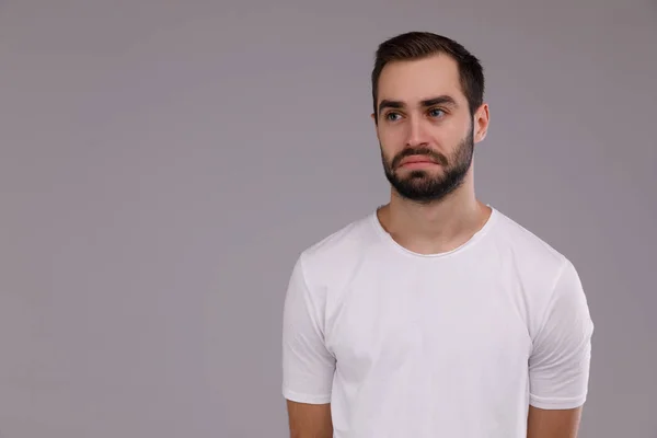 Retrato de um homem triste em uma camiseta branca em um fundo cinza . — Fotografia de Stock