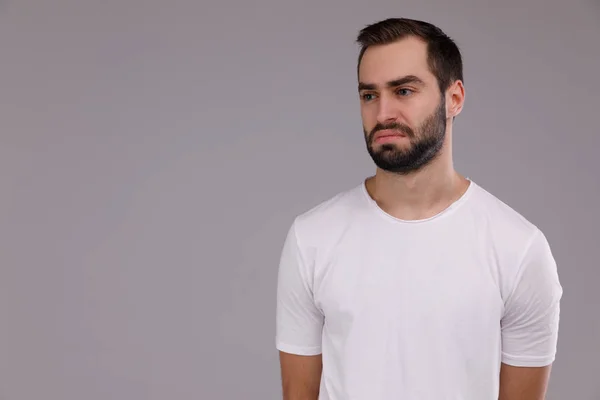 Retrato de um homem triste em uma camiseta branca em um fundo cinza . — Fotografia de Stock