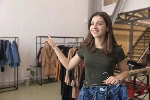 Дівчина в магазині вибирає джинси, дізнається, де роздягальня — стокове фото