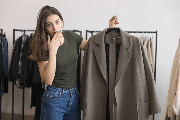 Mladá dívka v obchodě s oděvy vybere kabát. — Stock fotografie