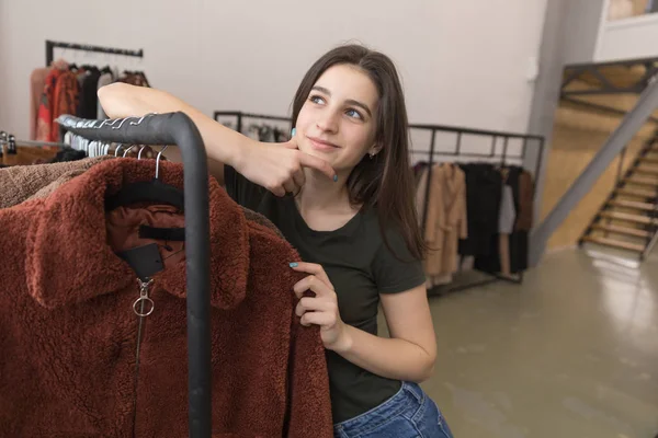 Dívka v obchodě s oděvy zvolí nový kožich. — Stock fotografie