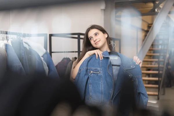 The girl in the clothing store chooses a denim jacket, chose and pressed to her. — Stock Photo, Image