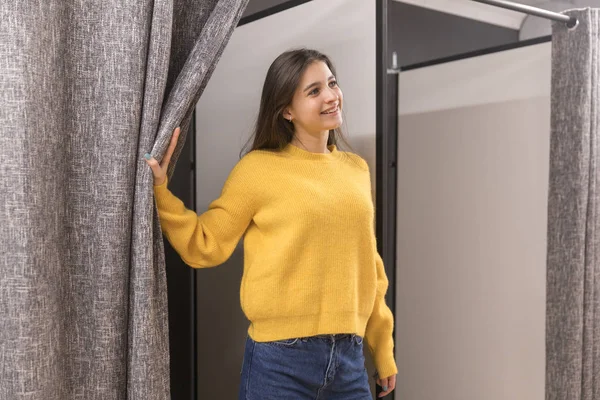 Jovencita en tienda de ropa probándose un suéter amarillo — Foto de Stock