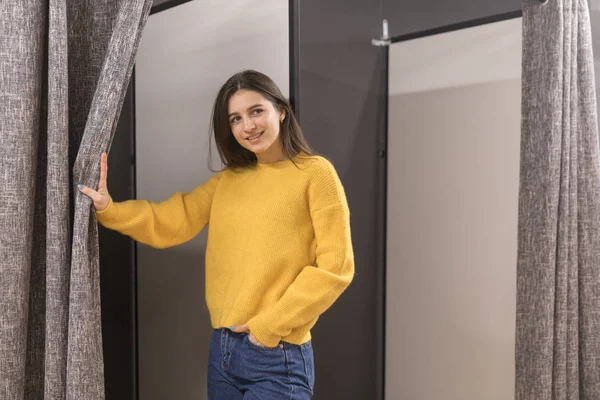 Jovencita en tienda de ropa probándose un suéter amarillo — Foto de Stock