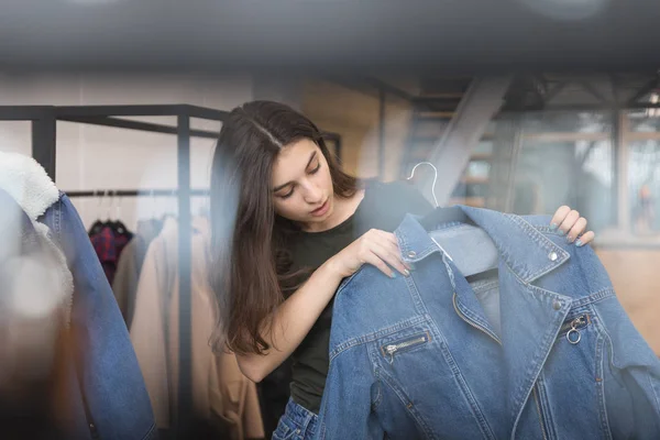 The girl in the clothing store chooses a denim jacket, looks at her. — Stock Photo, Image