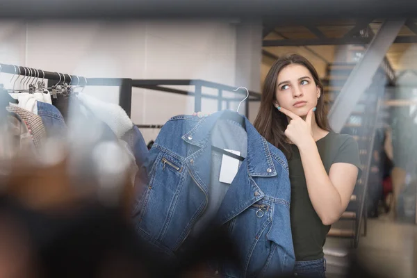 Крупним планом брюнетка в магазині думає, чи купити їй джинсову куртку — стокове фото