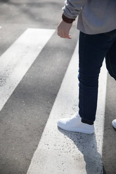 Joven en pantalones oscuros y zapatillas cruzando la calle — Foto de Stock