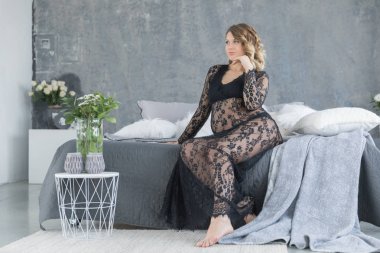 Hamile kadın yatakta oturup bir güzel dantel elbise