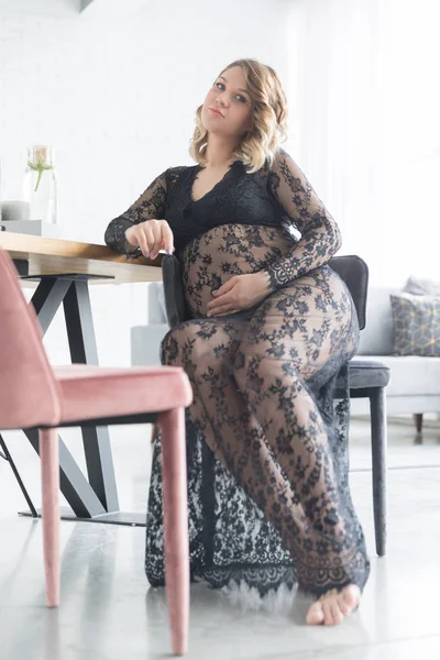 Hamile kadın güzel dantel elbise giymiş bir sandalyede oturur — Stok fotoğraf