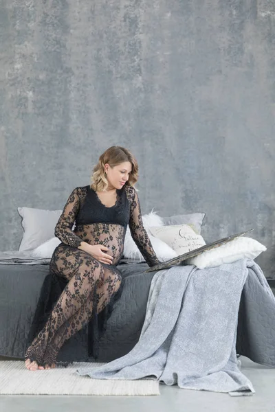 Zwangere vrouw in een prachtige lace jurk zittend op het bed — Stockfoto