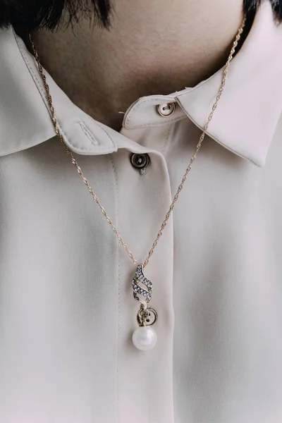 Close-up on the neck of the girl\'s precious chain with a pendant of pearls. Silver chain. The girl is wearing a white blouse.