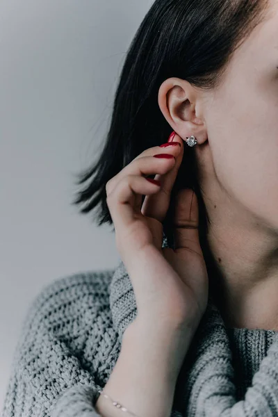 Close-up in the ear of the girl is a silver earring in the form of a small pebble, the earring is a carnation. Precious decoration.