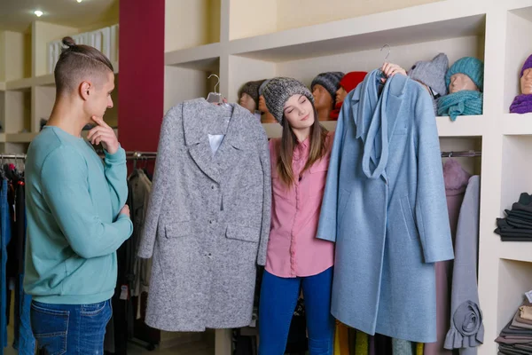 Ένα κορίτσι με ένα αγόρι στο μαγαζί διαλέγει το παλτό της.. — Φωτογραφία Αρχείου