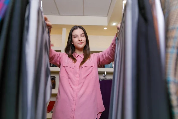 Close-up of a girl between clothes in a store. — Stock Photo, Image