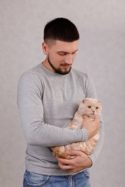 Genç adam sevimli kediyi elinde tutuyor.