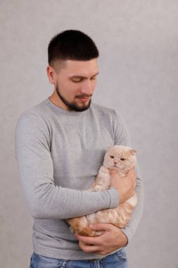 Genç adam sevimli kediyi elinde tutuyor.