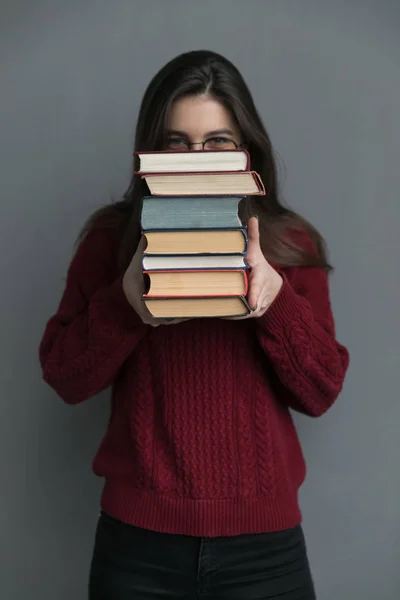 一个穿着红色毛衣的女孩手里拿着一本书的特写镜头 在她的脸上盖满了堆积如山的书籍 — 图库照片