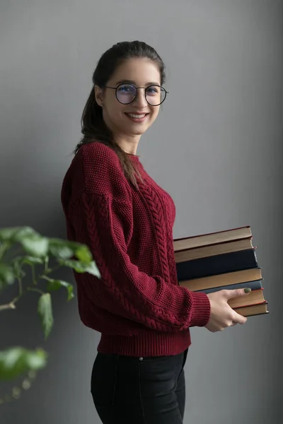 彼女の手に本を保持灰色の背景に 収集した髪を持つ少女の閉鎖 バーガンディのセーターとメガネを着て ストック写真